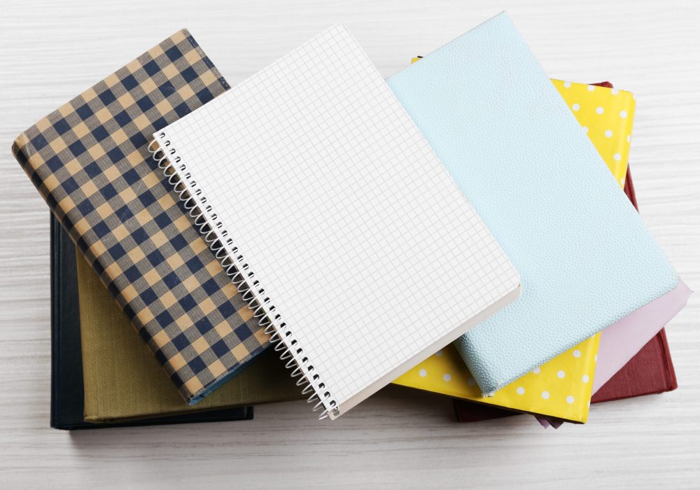 Notebook on top of pile of books and magazines on wooden background
