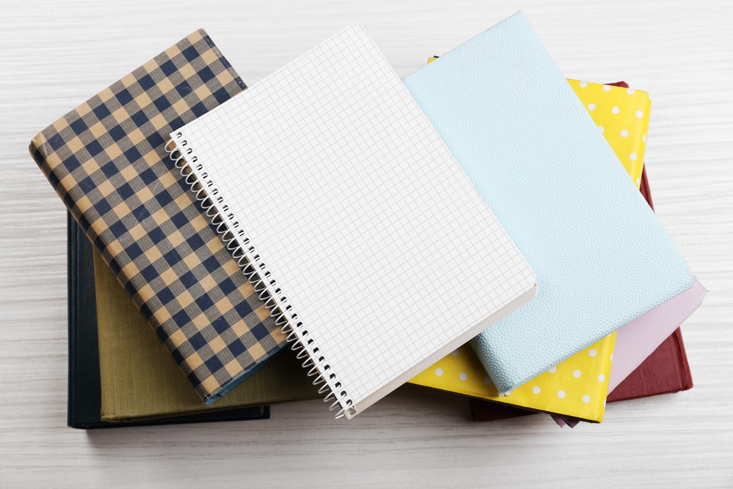 Notebook on top of pile of books and magazines on wooden background